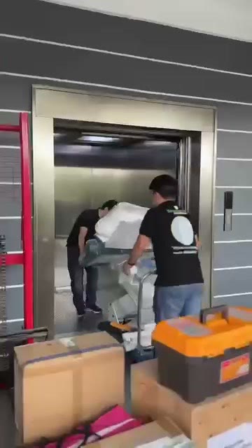 Two technicians wheeling the wrapped chair into the service lift