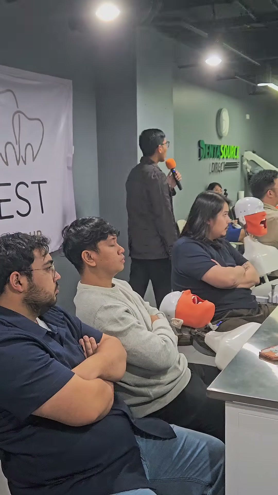 Dr. Emil at the microphone beside the banner as trainees work at their stations