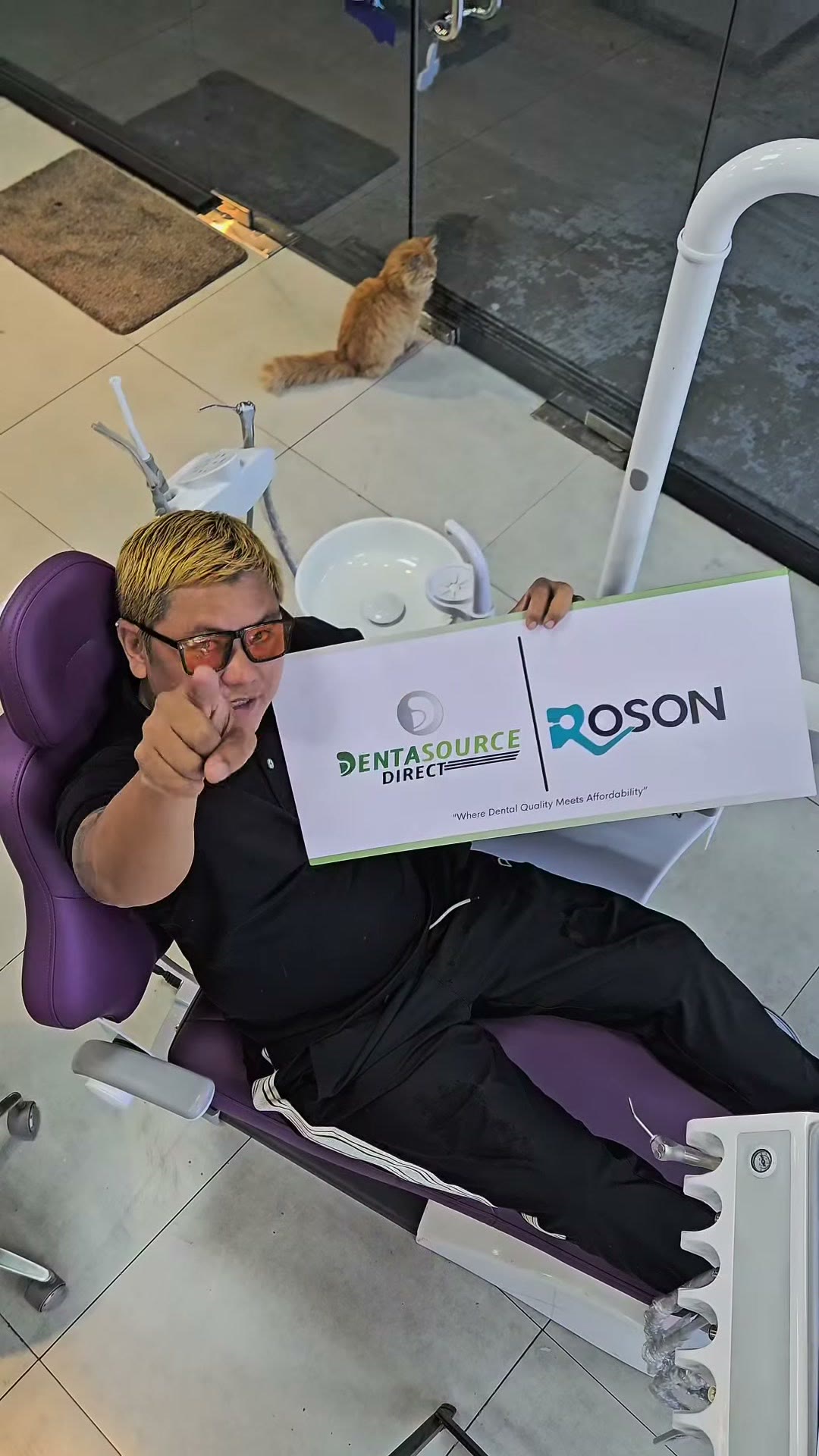 Reclining in a purple dental chair holding a DentaSource and ROSON board